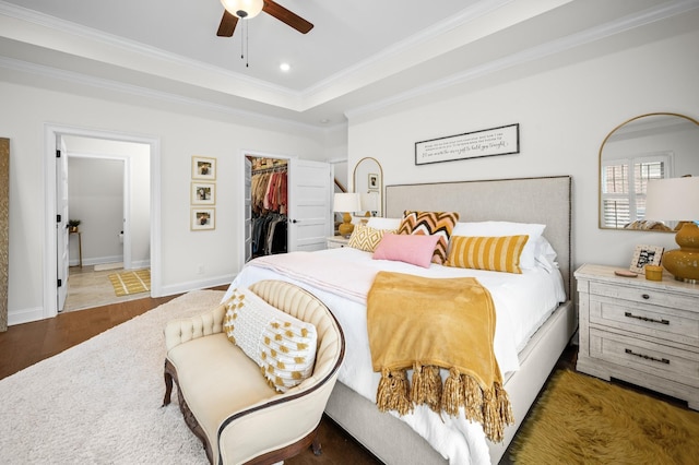 bedroom featuring a tray ceiling, recessed lighting, a spacious closet, ornamental molding, and wood finished floors