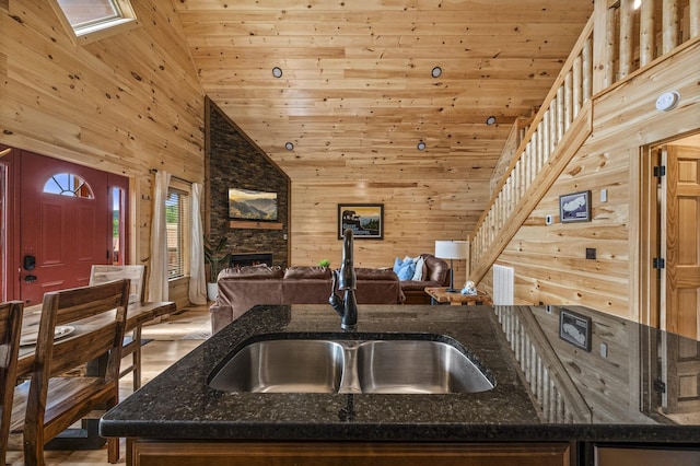 kitchen with wood walls, a fireplace, a sink, open floor plan, and dark stone counters