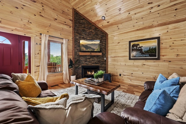 living room with wood ceiling, wooden walls, a stone fireplace, wood finished floors, and high vaulted ceiling