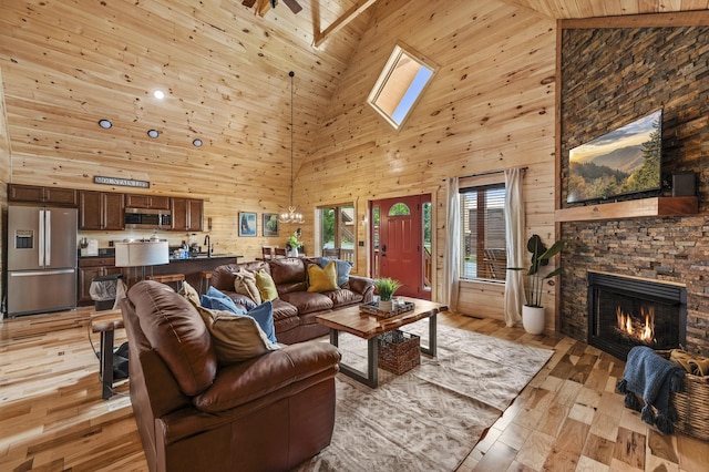 living area featuring light wood-style floors, wood walls, a stone fireplace, and lofted ceiling with skylight