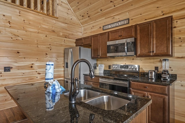 kitchen with lofted ceiling, a kitchen island with sink, stainless steel appliances, wood walls, and a sink