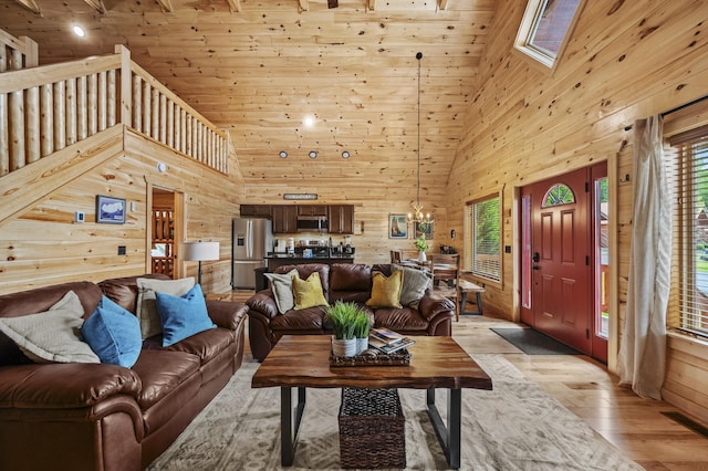 living room featuring high vaulted ceiling, wood walls, light wood-type flooring, and a skylight