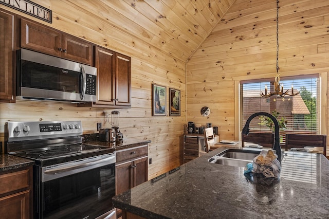 kitchen with pendant lighting, lofted ceiling, appliances with stainless steel finishes, a sink, and wooden walls