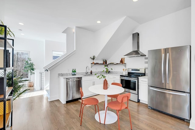 kitchen with a sink, white cabinetry, light countertops, appliances with stainless steel finishes, and wall chimney range hood