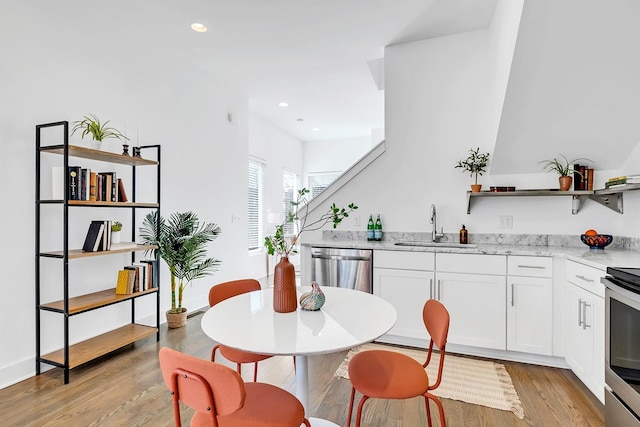 kitchen featuring open shelves, appliances with stainless steel finishes, a sink, and light wood-style floors