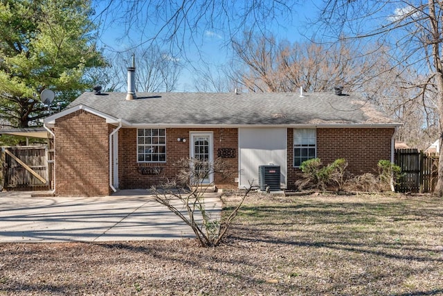 back of house featuring central AC, brick siding, fence, roof with shingles, and a lawn