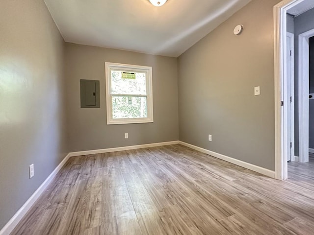 spare room with electric panel, baseboards, and wood finished floors