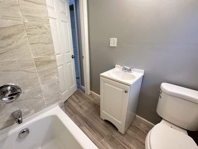 bathroom featuring a bathtub, toilet, vanity, wood finished floors, and baseboards