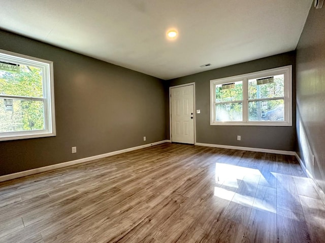 empty room featuring wood finished floors, visible vents, and baseboards