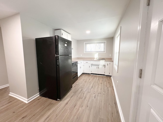 kitchen with light wood finished floors, light countertops, white cabinets, black appliances, and baseboards