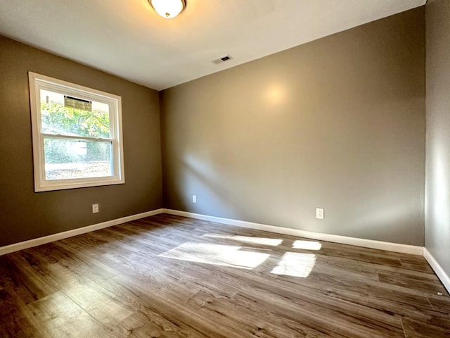 empty room with wood finished floors, visible vents, and baseboards