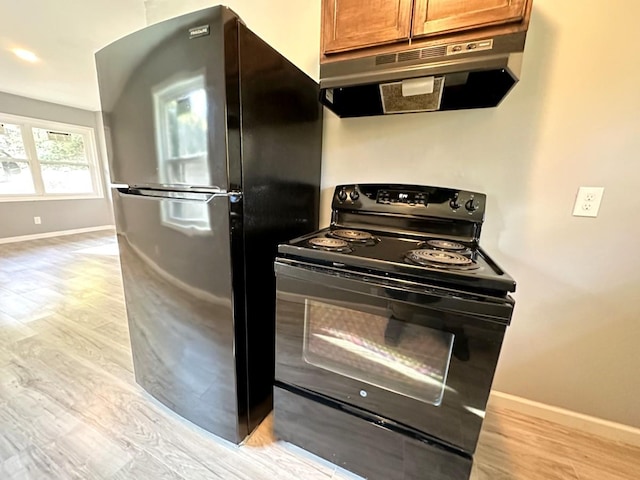 kitchen with light wood-type flooring, freestanding refrigerator, black electric range oven, and under cabinet range hood