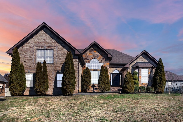 french country home with brick siding, stone siding, and a front lawn