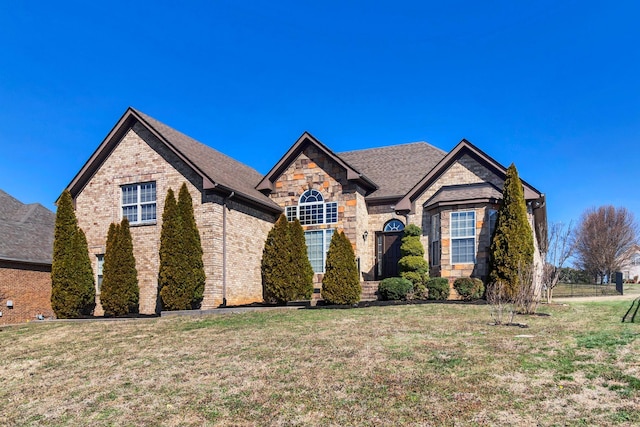 view of front of house with stone siding, brick siding, roof with shingles, and a front yard