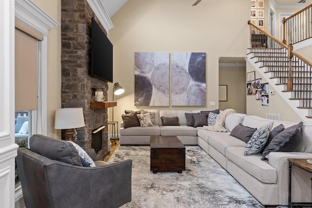 living room featuring a high ceiling, a fireplace, visible vents, ornamental molding, and stairway