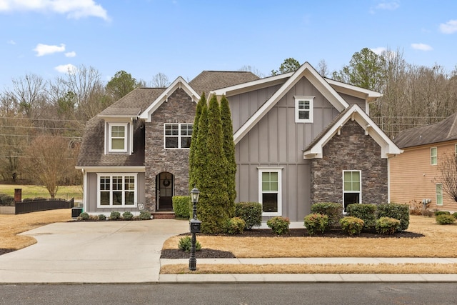 view of front of house featuring driveway, stone siding, a shingled roof, and board and batten siding