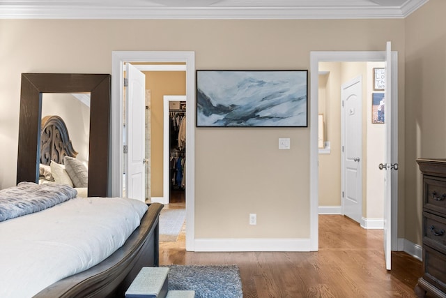 bedroom with baseboards, ornamental molding, wood finished floors, a walk in closet, and a closet