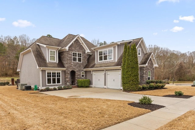 view of front facade with cooling unit, a garage, stone siding, concrete driveway, and roof with shingles