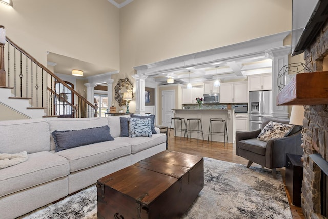 living room featuring coffered ceiling, wood finished floors, ornamental molding, stairway, and ornate columns