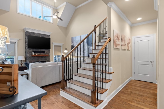 staircase with a fireplace, a ceiling fan, ornamental molding, wood finished floors, and baseboards