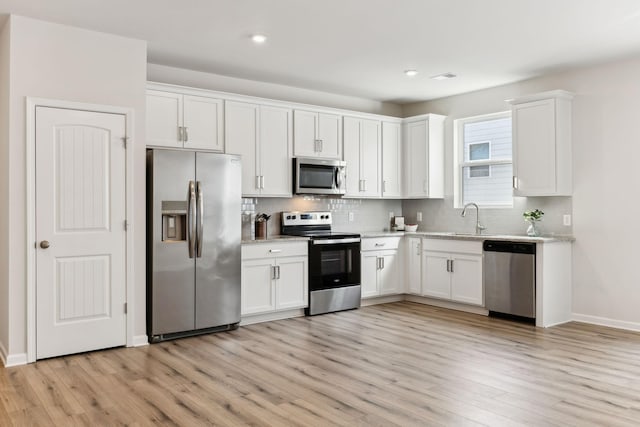 kitchen with decorative backsplash, stainless steel appliances, light wood-style floors, white cabinetry, and a sink