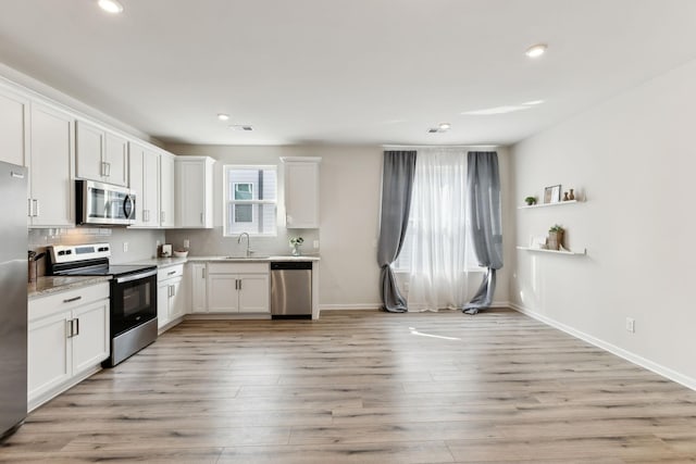 kitchen with appliances with stainless steel finishes, backsplash, a sink, and light wood-style floors