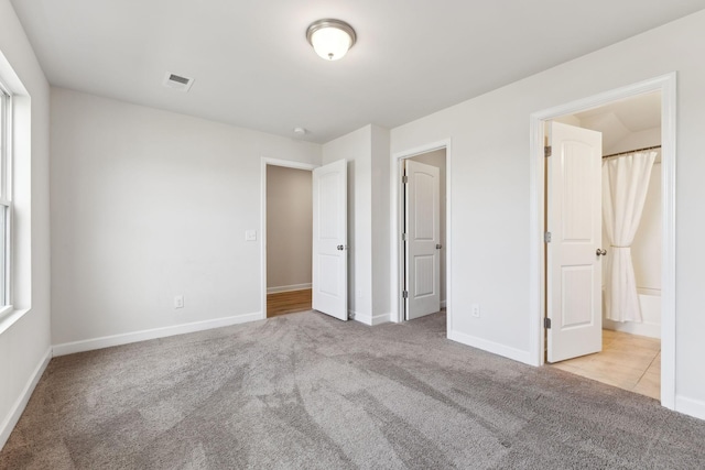 unfurnished bedroom with carpet floors, ensuite bath, visible vents, and baseboards