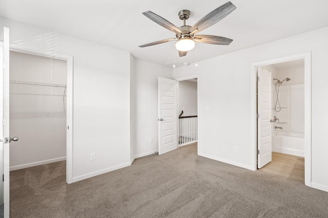 unfurnished bedroom featuring a walk in closet, carpet flooring, connected bathroom, ceiling fan, and baseboards