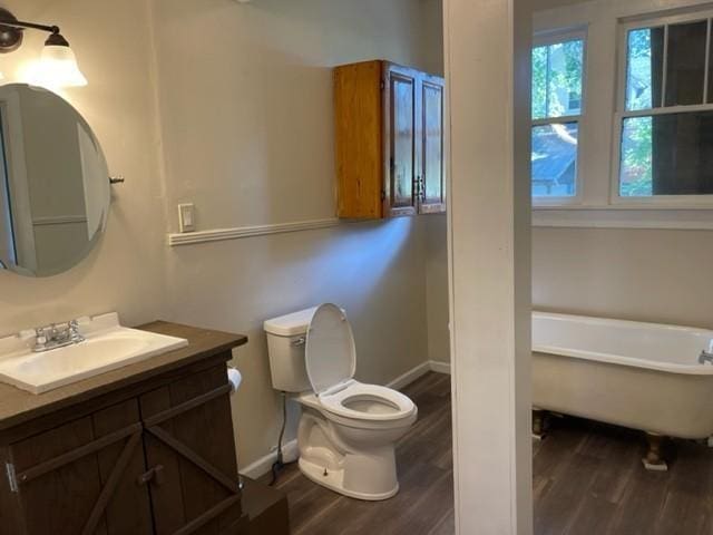 full bath with toilet, a freestanding tub, wood finished floors, and vanity