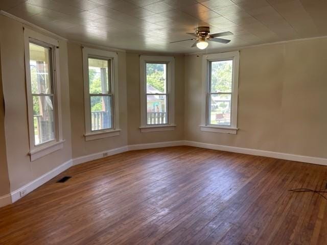 spare room featuring visible vents, ornamental molding, ceiling fan, wood finished floors, and baseboards