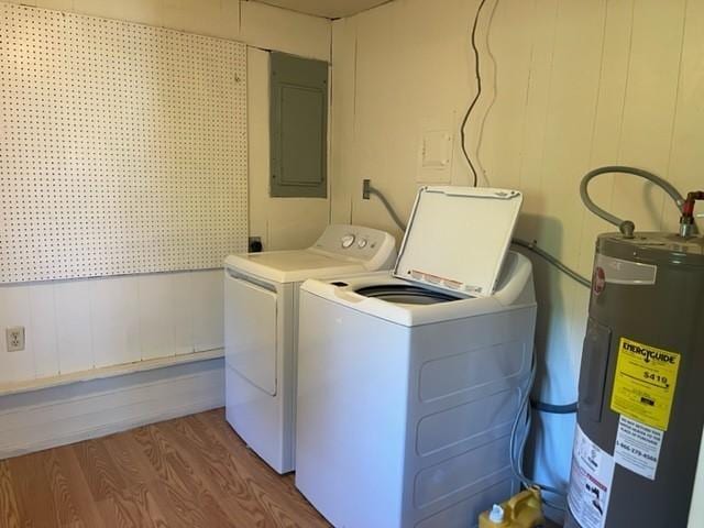 washroom with laundry area, electric panel, washer and clothes dryer, wood finished floors, and water heater