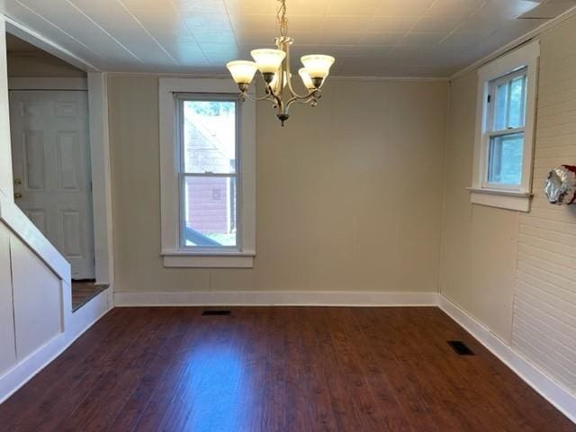 unfurnished dining area featuring dark wood-type flooring, an inviting chandelier, visible vents, and baseboards