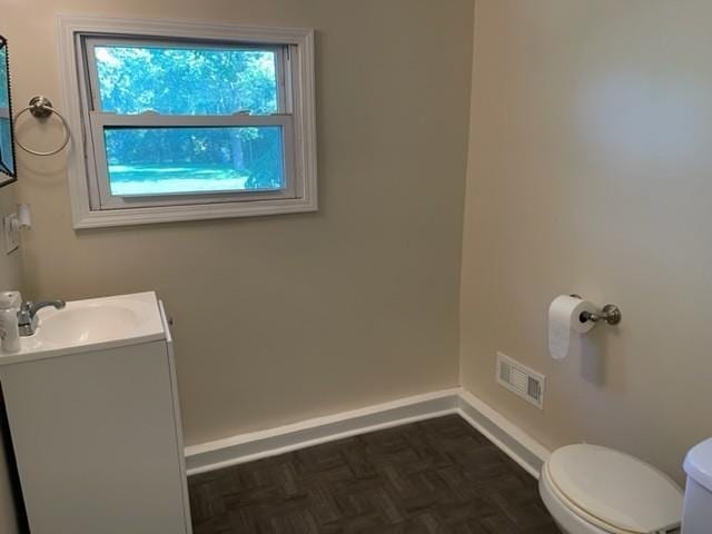 half bathroom featuring baseboards, visible vents, vanity, and toilet