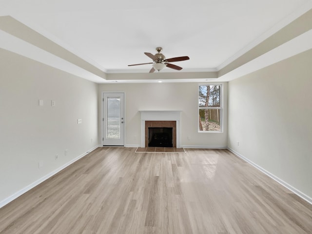 unfurnished living room with light wood-style floors, a tray ceiling, a fireplace, and baseboards