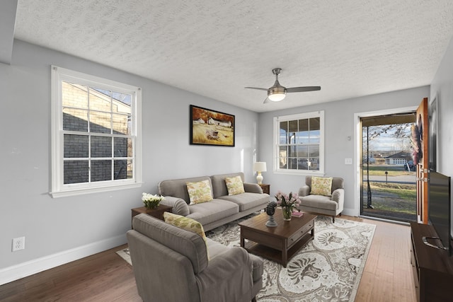 living area with ceiling fan, a textured ceiling, baseboards, and wood finished floors