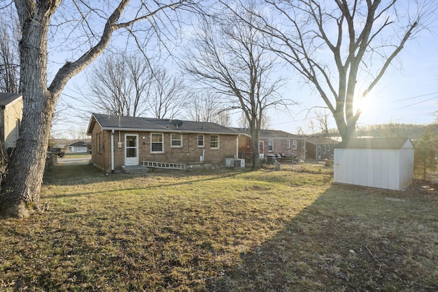 rear view of property with central AC, brick siding, an outdoor structure, a yard, and a storage unit