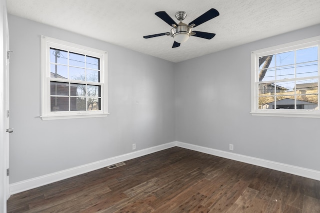 empty room featuring dark wood-type flooring, visible vents, and a healthy amount of sunlight