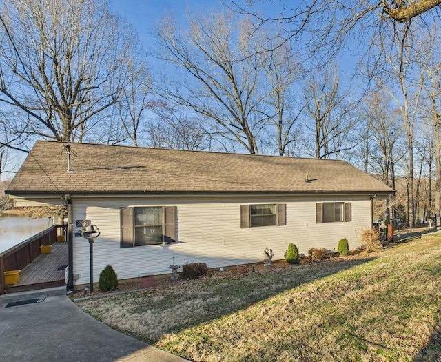 view of front of house featuring a shingled roof, a front lawn, and a deck with water view