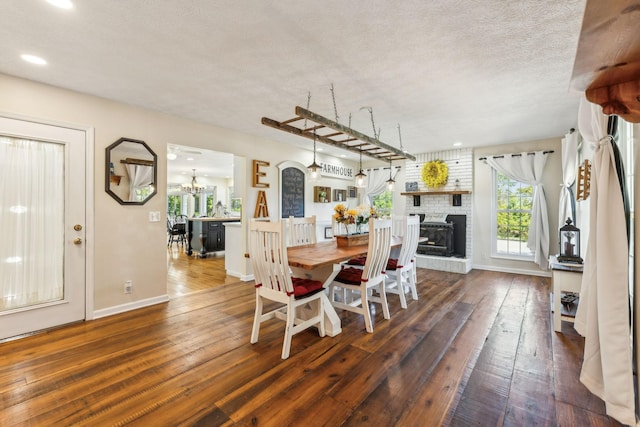 dining room with a chandelier, a textured ceiling, dark wood-type flooring, baseboards, and a brick fireplace