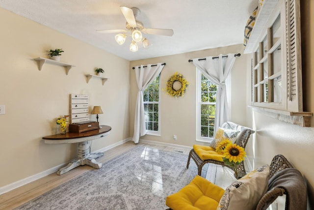 living area with a ceiling fan, baseboards, and wood finished floors