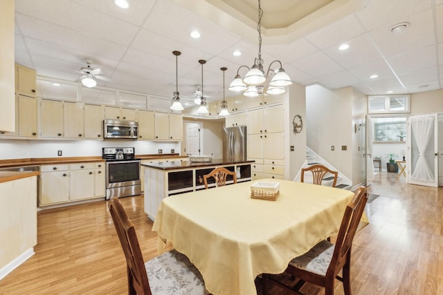 dining space with light wood-style floors, a ceiling fan, a drop ceiling, and stairs