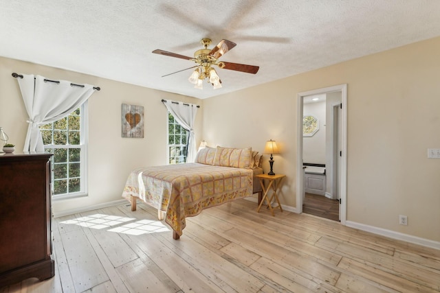 bedroom with light wood-style floors, a ceiling fan, a textured ceiling, ensuite bath, and baseboards