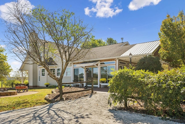 rear view of property featuring a patio, an outdoor fire pit, a sunroom, a standing seam roof, and metal roof