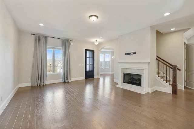 unfurnished living room featuring a tile fireplace, recessed lighting, wood finished floors, baseboards, and stairway