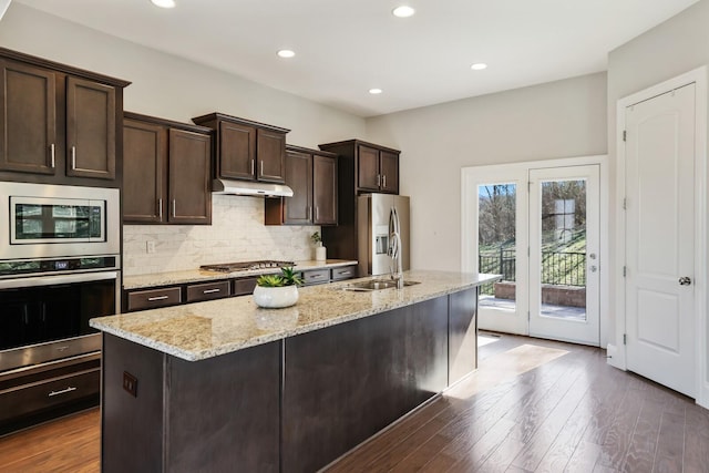 kitchen with under cabinet range hood, stainless steel appliances, a sink, dark brown cabinets, and tasteful backsplash