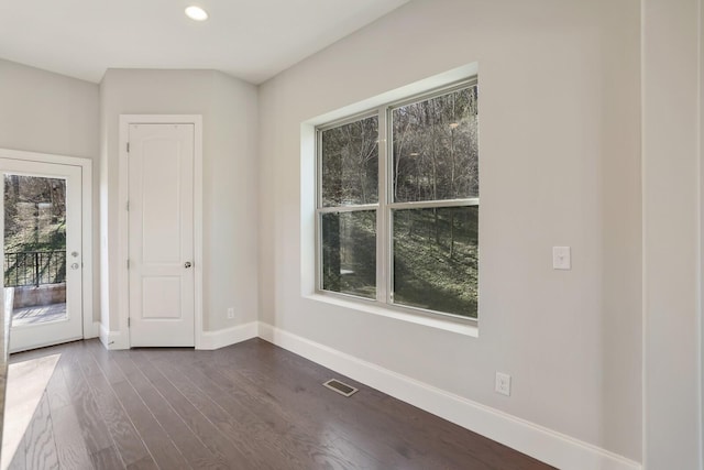 spare room featuring dark wood-style floors, plenty of natural light, visible vents, and baseboards