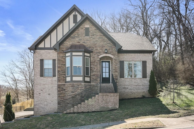 tudor home featuring brick siding, roof with shingles, fence, a front lawn, and stucco siding