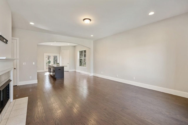 unfurnished living room featuring arched walkways, a tile fireplace, recessed lighting, baseboards, and dark wood finished floors