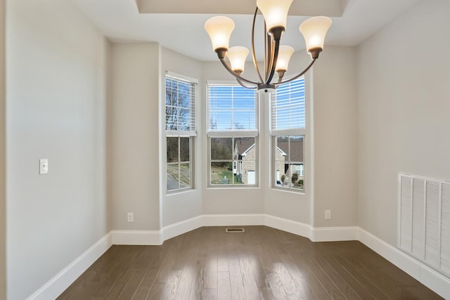 unfurnished dining area featuring dark wood-style flooring, visible vents, a notable chandelier, and baseboards