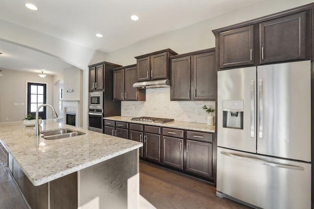 kitchen with dark brown cabinetry, arched walkways, appliances with stainless steel finishes, under cabinet range hood, and a sink